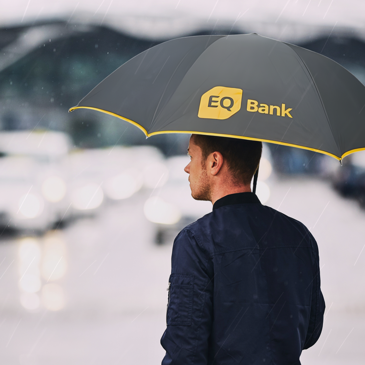 Man holding an umbrella with EQ Bank logo in a rainy setting